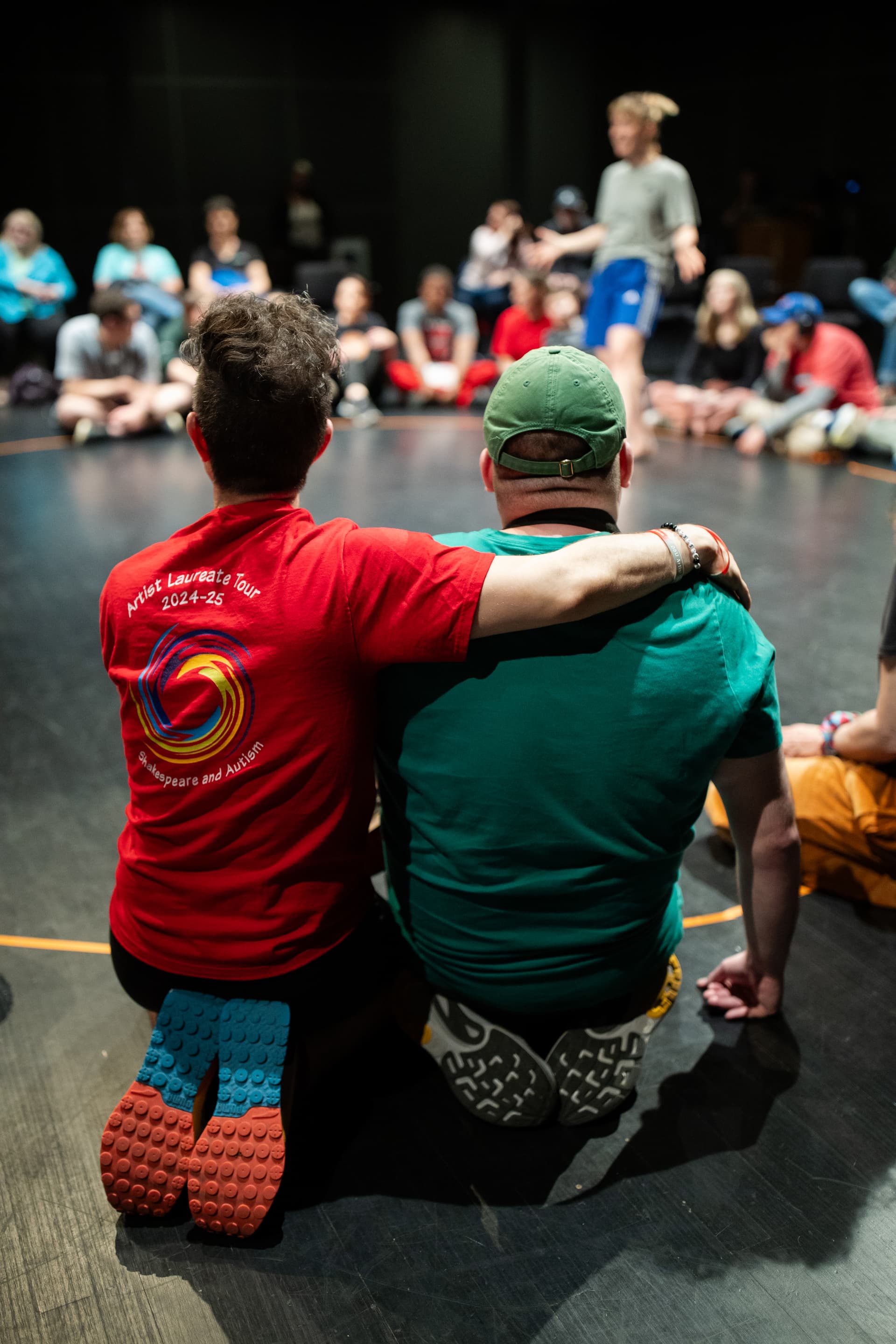 Shakespeare and Autism 2025 workshop participants seated in a circle, with one person’s arm around another in a moment of connection and inclusion.