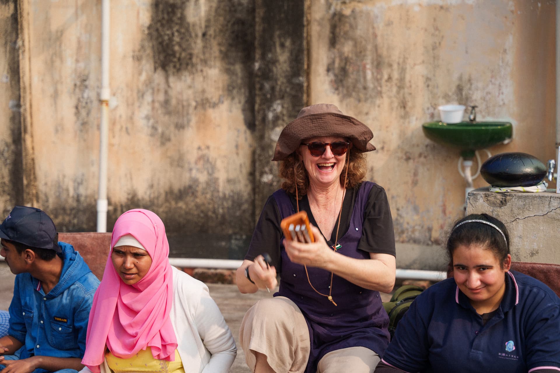 Kelly Hunter MBE smiling warmly in sunlight, seated outdoors. Founder of Flute Theatre, she develops groundbreaking Shakespeare adaptations for autistic individuals and neurodivergent audiences.
