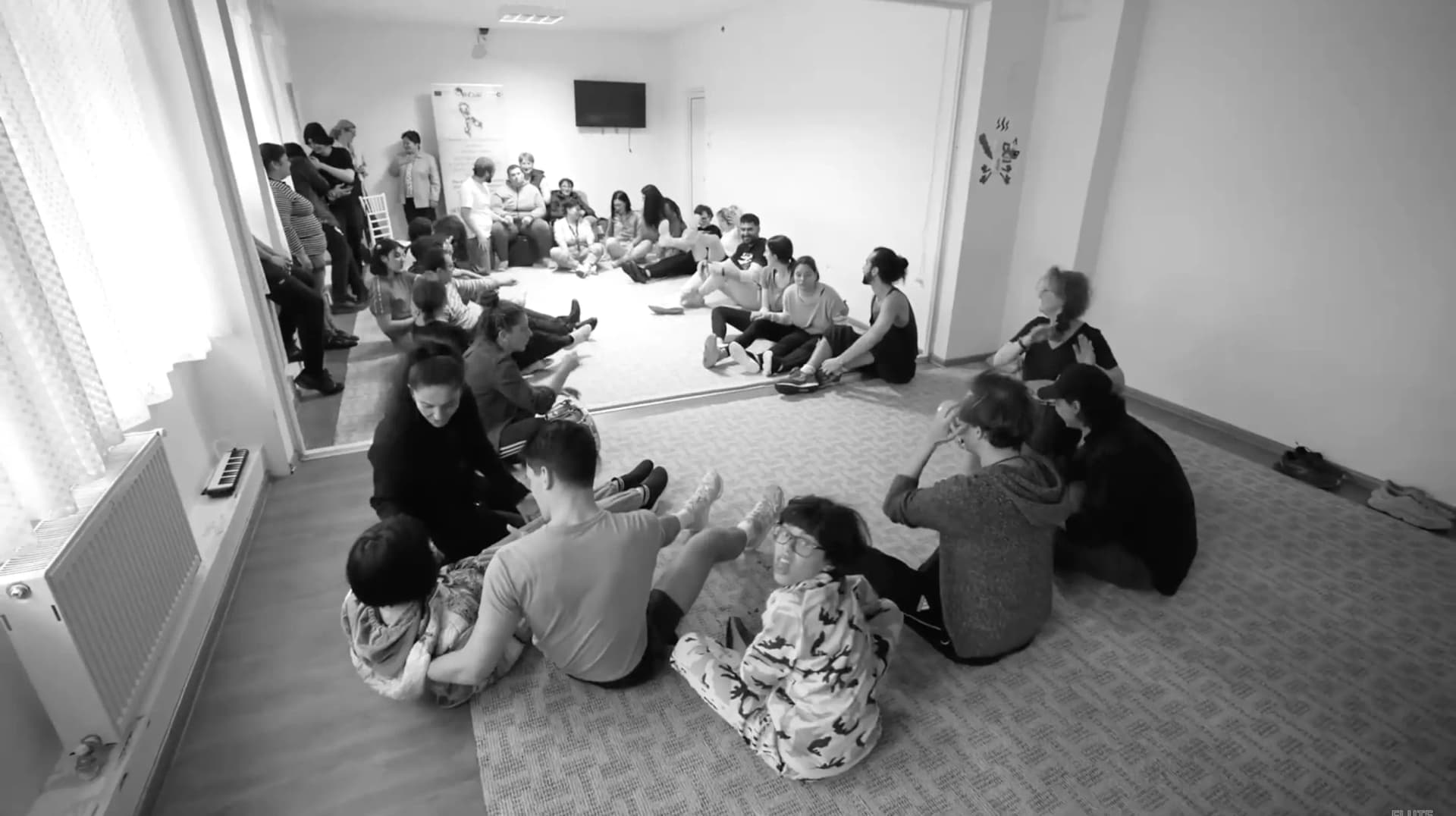 Black-and-white photo of a group of autistic participants, families, and Flute Theatre actors sitting in a circle during an interactive session at the Craiova Shakespeare Festival in Romania (2023).