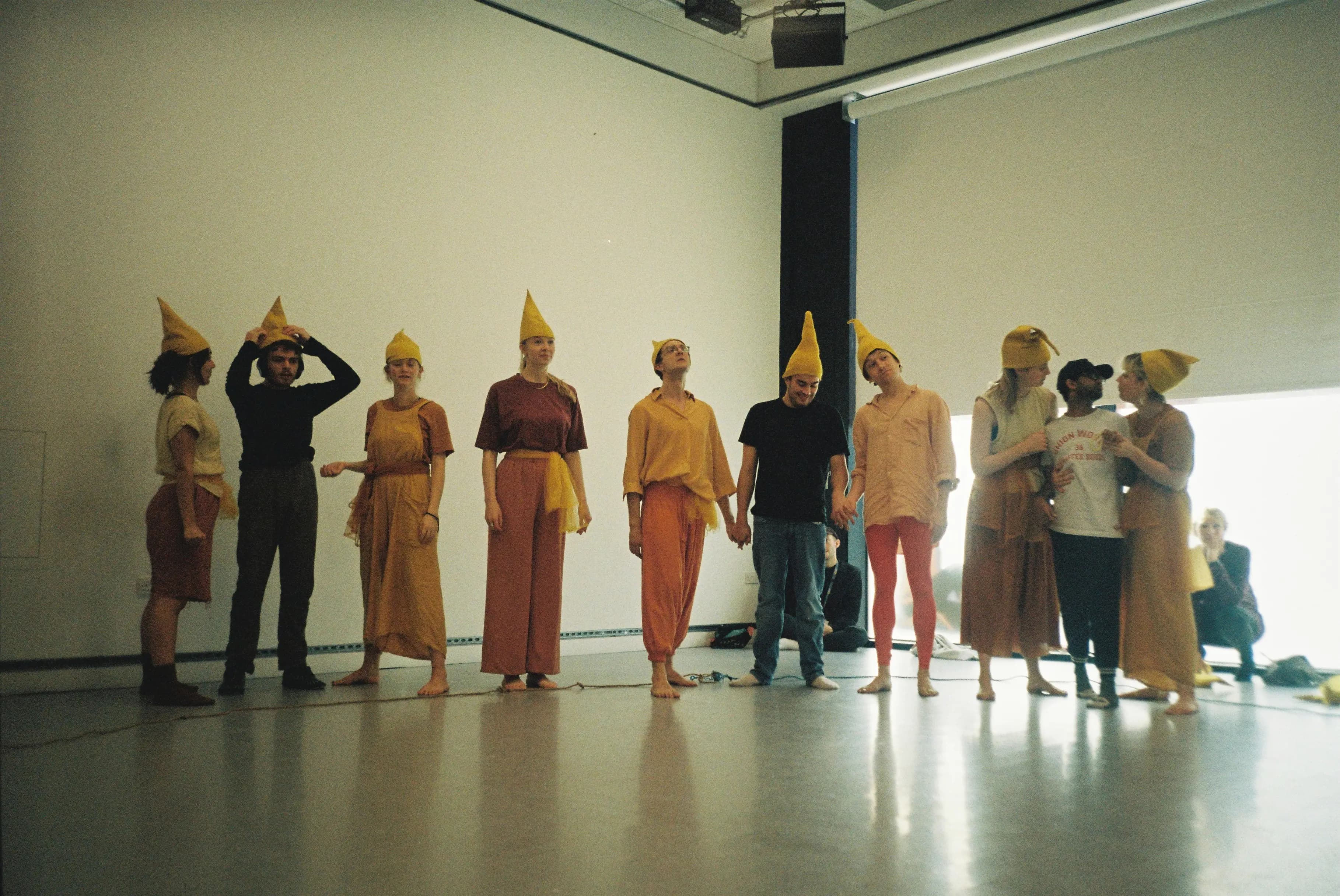 Autistic and neurotypical performers wearing yellow hats and colourful costumes standing in a line during a Hunter Heartbeat Method workshop by Flute Theatre, using Shakespeare to connect through rhythm, gesture, and play.