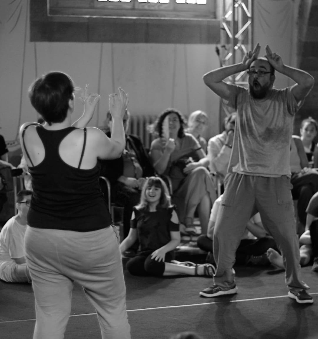 Pep and Anna playfully mimic animal gestures during a theatre performance in Granollers, Catalunya, 2019, as the audience smiles and watches.