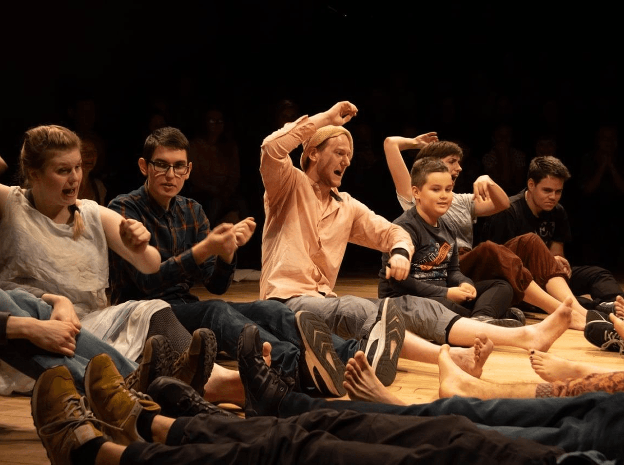 A diverse group of actors and autistic participants sit in a circle, enthusiastically mirroring gestures in a group activity. This scene represents a signature exercise from the Hunter Heartbeat Method, designed to foster connection through rhythm, breath, and interaction.