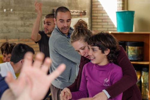 A young girl in a purple top is gently embraced from behind by another participant, both smiling softly, during a supportive session at Montserrat Montero Special Education Centre in Granollers.