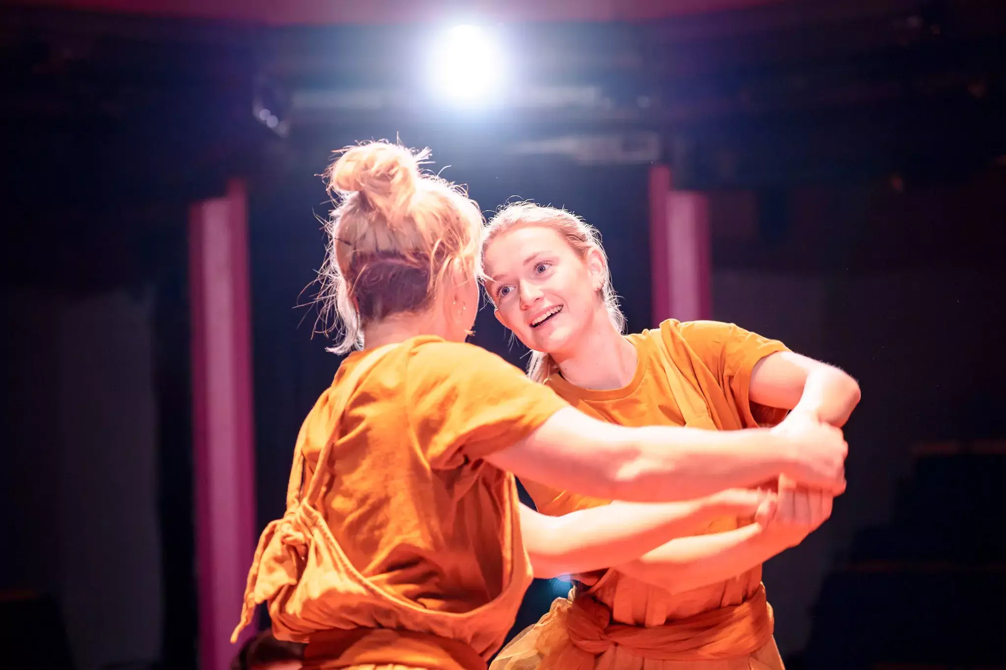Two actors in orange costumes joyfully holding hands and connecting through eye contact during a sensory-friendly performance of Twelfth Night by Flute Theatre, using the Hunter Heartbeat Method to engage autistic participants through Shakespeare.