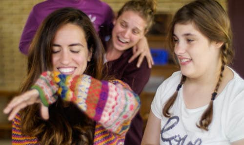A young woman in a colorful striped sweater laughs joyfully with two other girls, enjoying an engaging and inclusive activity at Montserrat Montero Special Education Centre in Granollers.