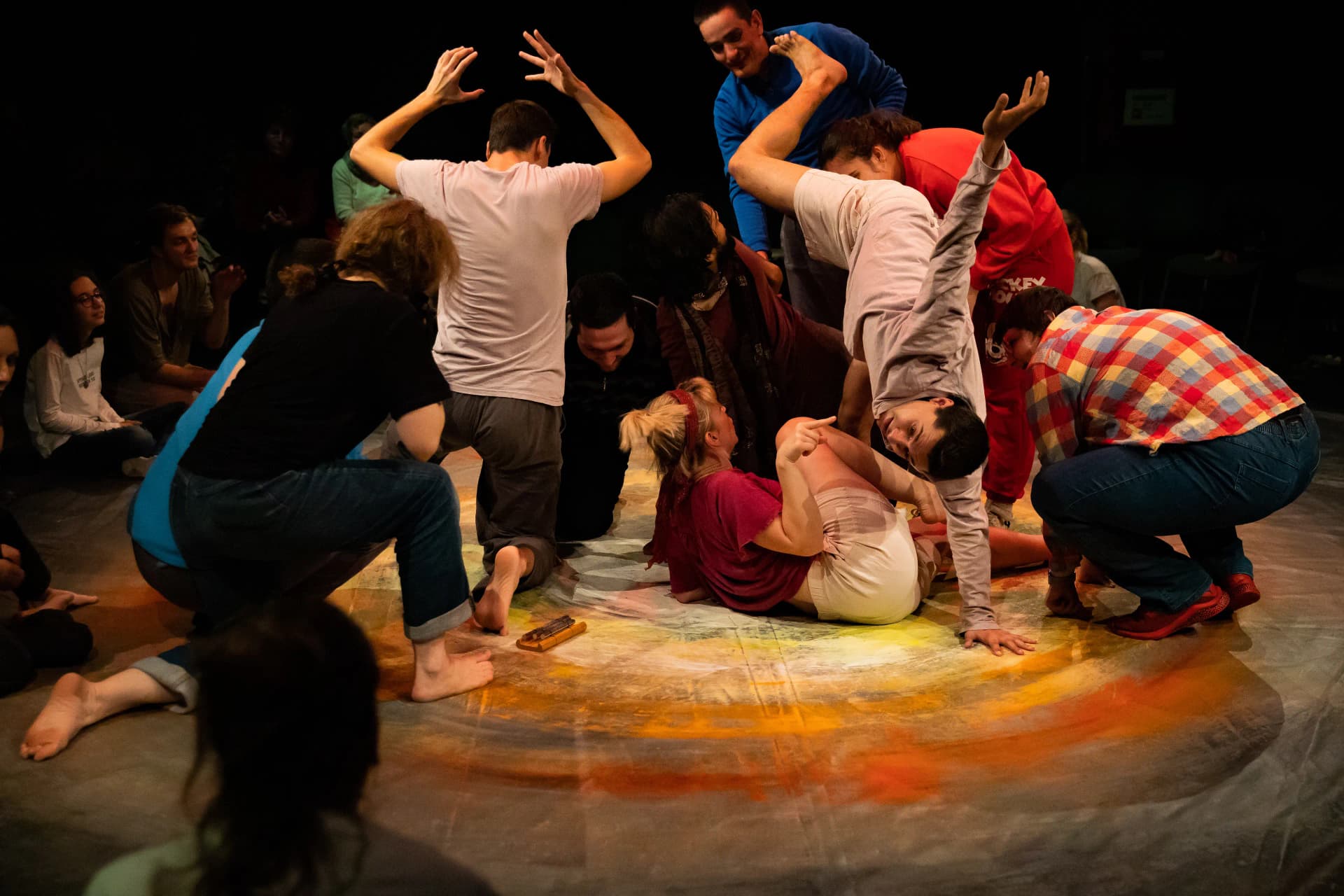 Performers and participants at the Teatrul Gong in Sibiu in 2023 engaging in a collaborative movement workshop. They are gathered on a colourful circular stage, with some standing, crouching, and lying on the floor, creating an expressive and dynamic group formation
