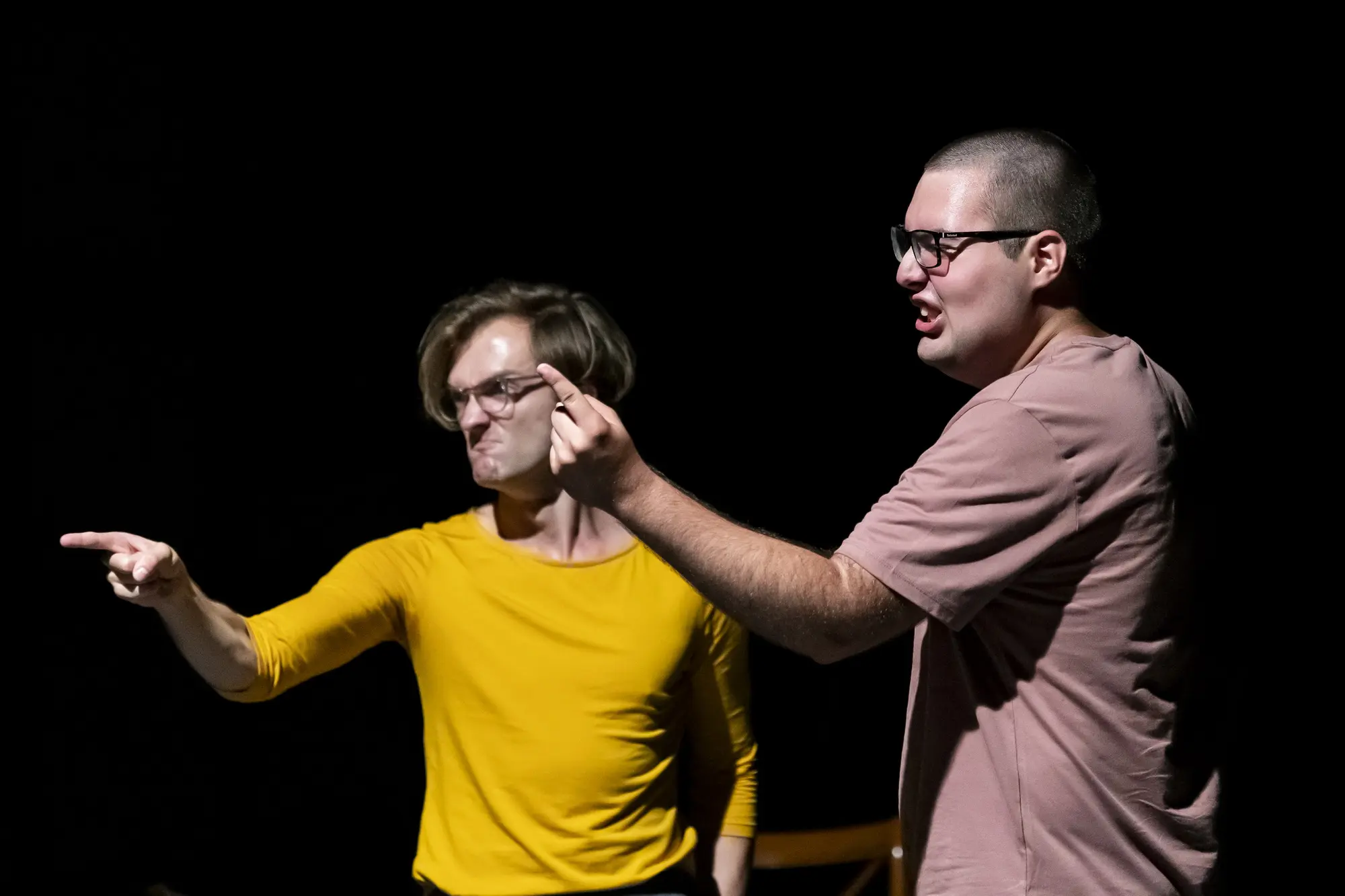Two performers, one in a bright yellow shirt and the other in pink, gesture passionately and point during an animated storytelling moment.