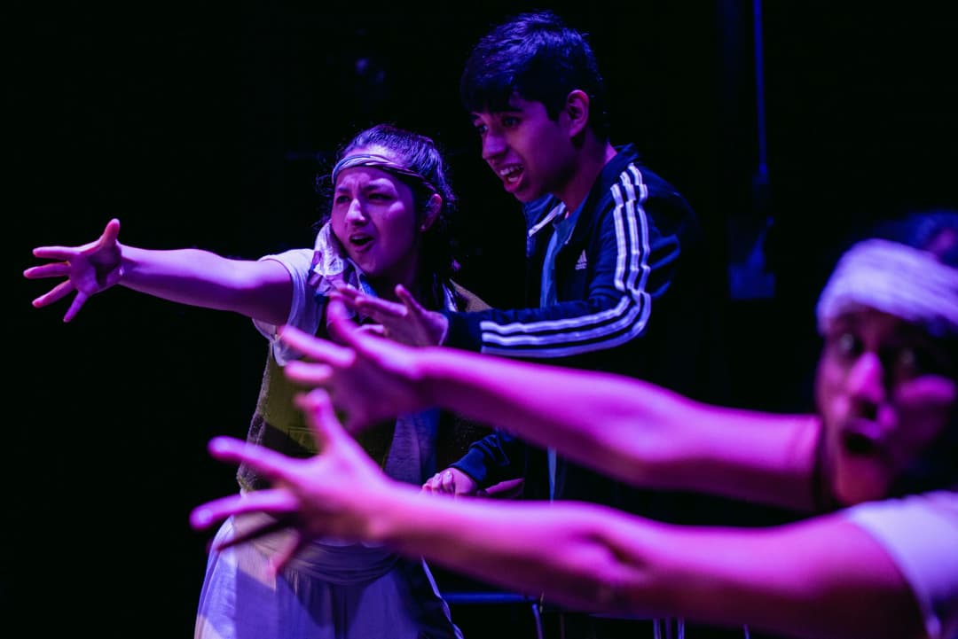 Two young performers reaching out with expressive gestures in an emotional theatre moment at Teatro La Plaza in Peru.