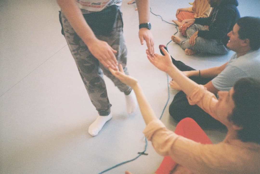 A person standing and gently reaching out to touch the hands of seated participants during a sensory movement workshop in Brighton, fostering connection and engagement.
