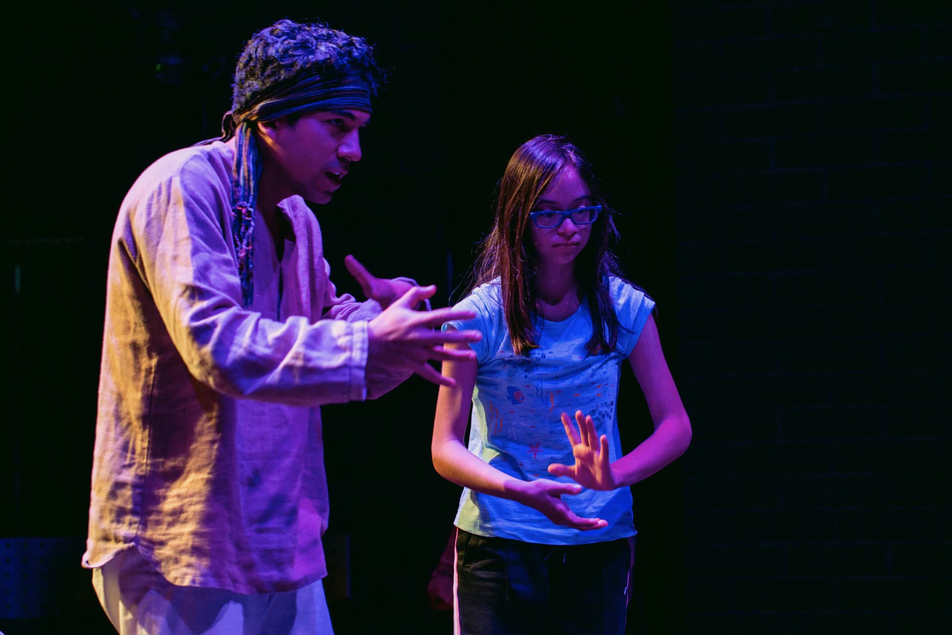 An actor and a young girl concentrating on a theatrical exercise on stage in Peru, illuminated by dramatic lighting.
