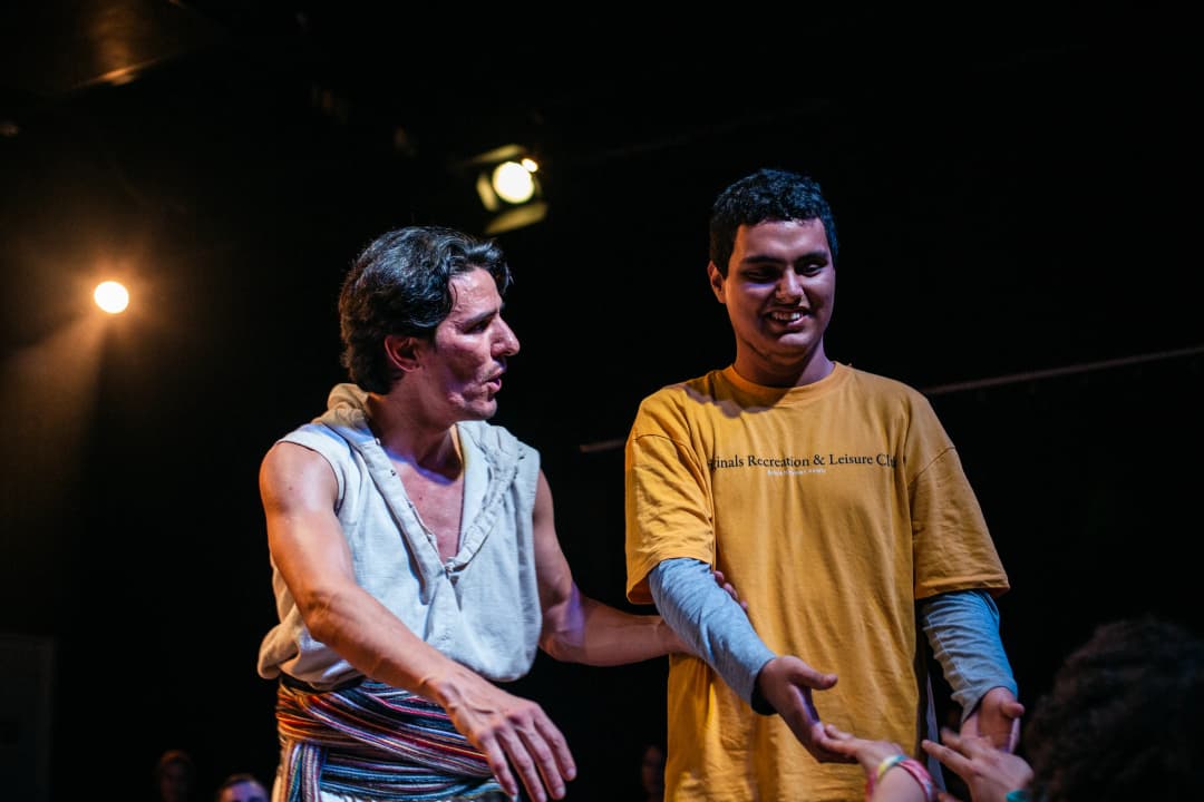A smiling young man interacts with a performer in a warm, inclusive moment under soft stage lighting.