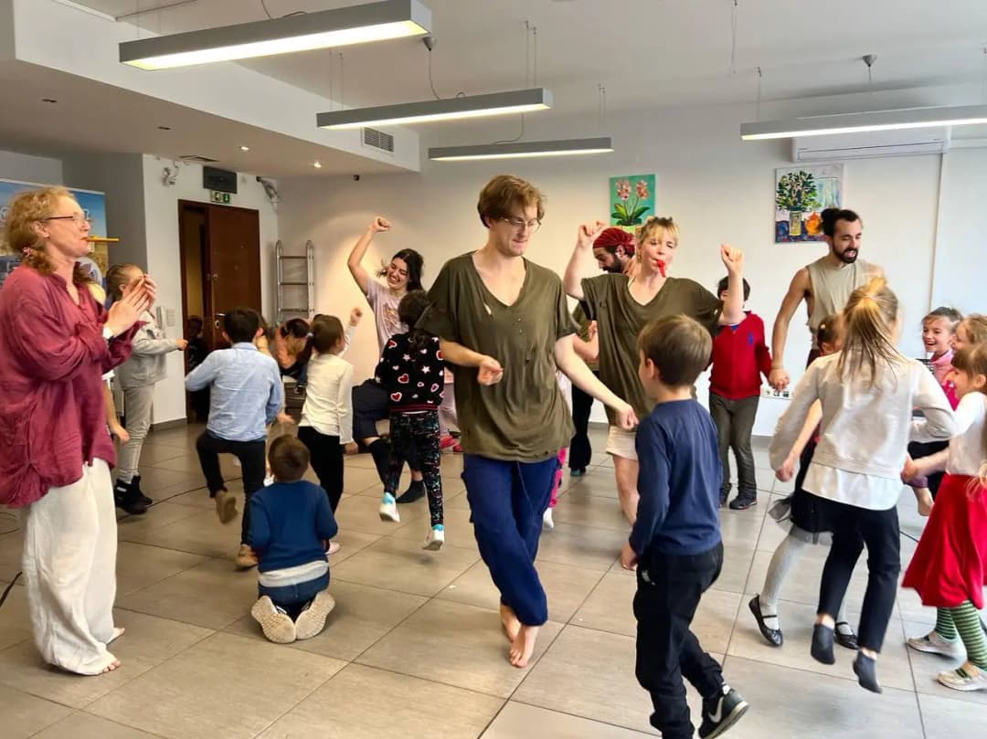 A lively scene of performers and children dancing joyfully together in a bright room with modern lighting and artwork on the walls.
