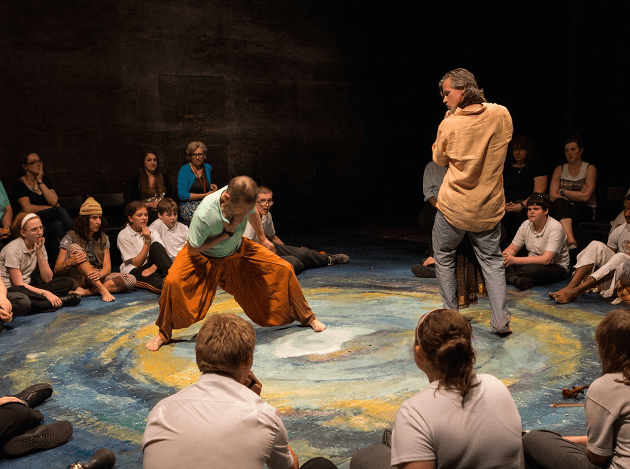 An inclusive performance by Flute Theatre, where actors and autistic participants sit together in a circular space painted with a swirling galaxy design. This moment captures an adaptation of Shakespeare using the Hunter Heartbeat method—a sensory drama technique created to engage autistic individuals through rhythm, breath, and connection. Flute Theatre provides these powerful, interactive performances alongside training for actors, teachers, family members, and applied theatre students.