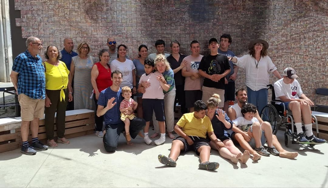 Catalan families at Arsènic, Espai de Creació in Granollers, 2025. A joyful group of autistic children, their families, and Flute Theatre facilitators pose together outdoors against a mosaic wall, celebrating an inclusive Shakespeare workshop experience in Catalunya.