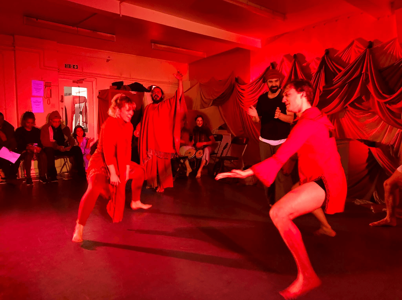Actors dressed in red move dynamically across the floor in a warm, immersive space, surrounded by an audience. This performance by Flute Theatre uses sensory-rich design and movement to make Shakespeare’s language accessible and inclusive.