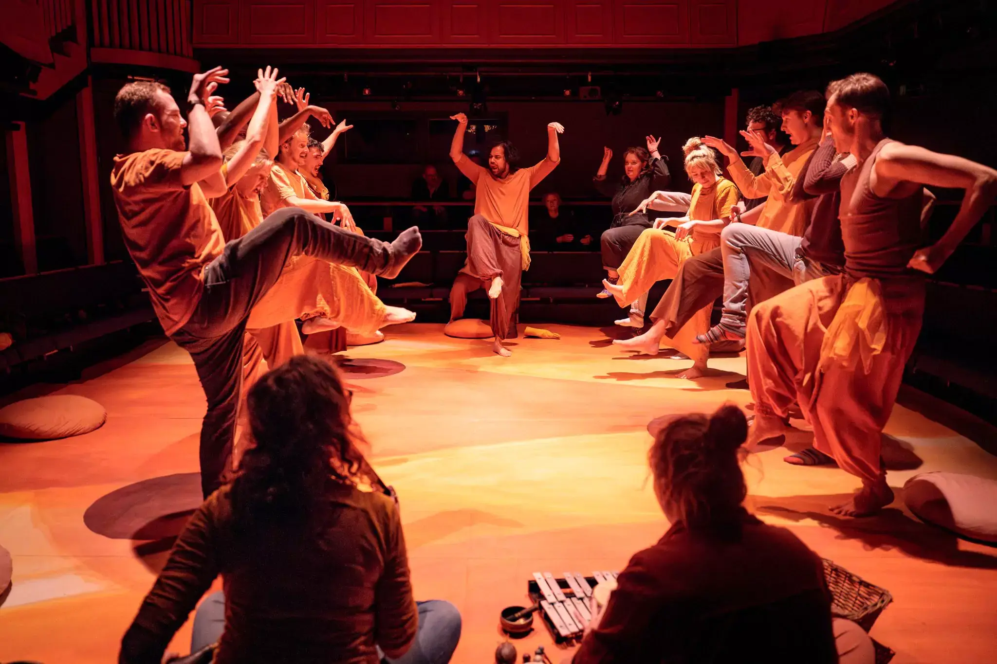 Cast and autistic participants of Flute Theatre’s Twelfth Night stand in a circle with raised arms and lifted legs, engaging in a synchronised movement game using the Hunter Heartbeat Method to foster connection and play through Shakespeare.