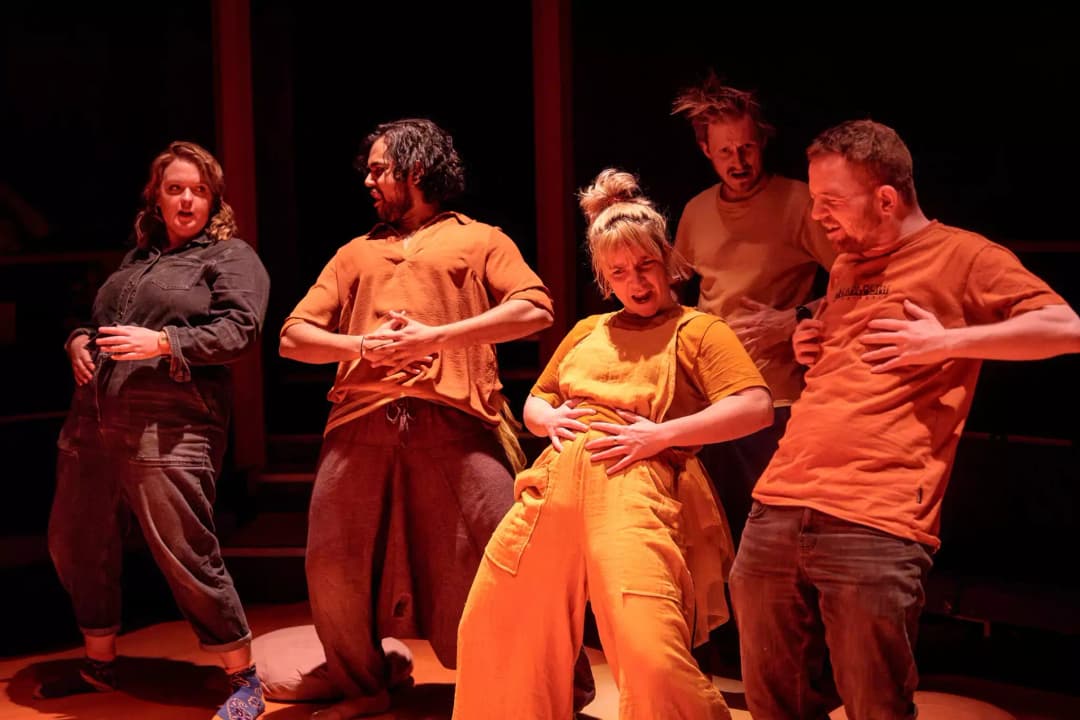 A group of Flute Theatre performers laugh and mime exaggerated belly gestures during an interactive scene from Twelfth Night, inviting autistic audience members to join through shared rhythm and physical comedy.